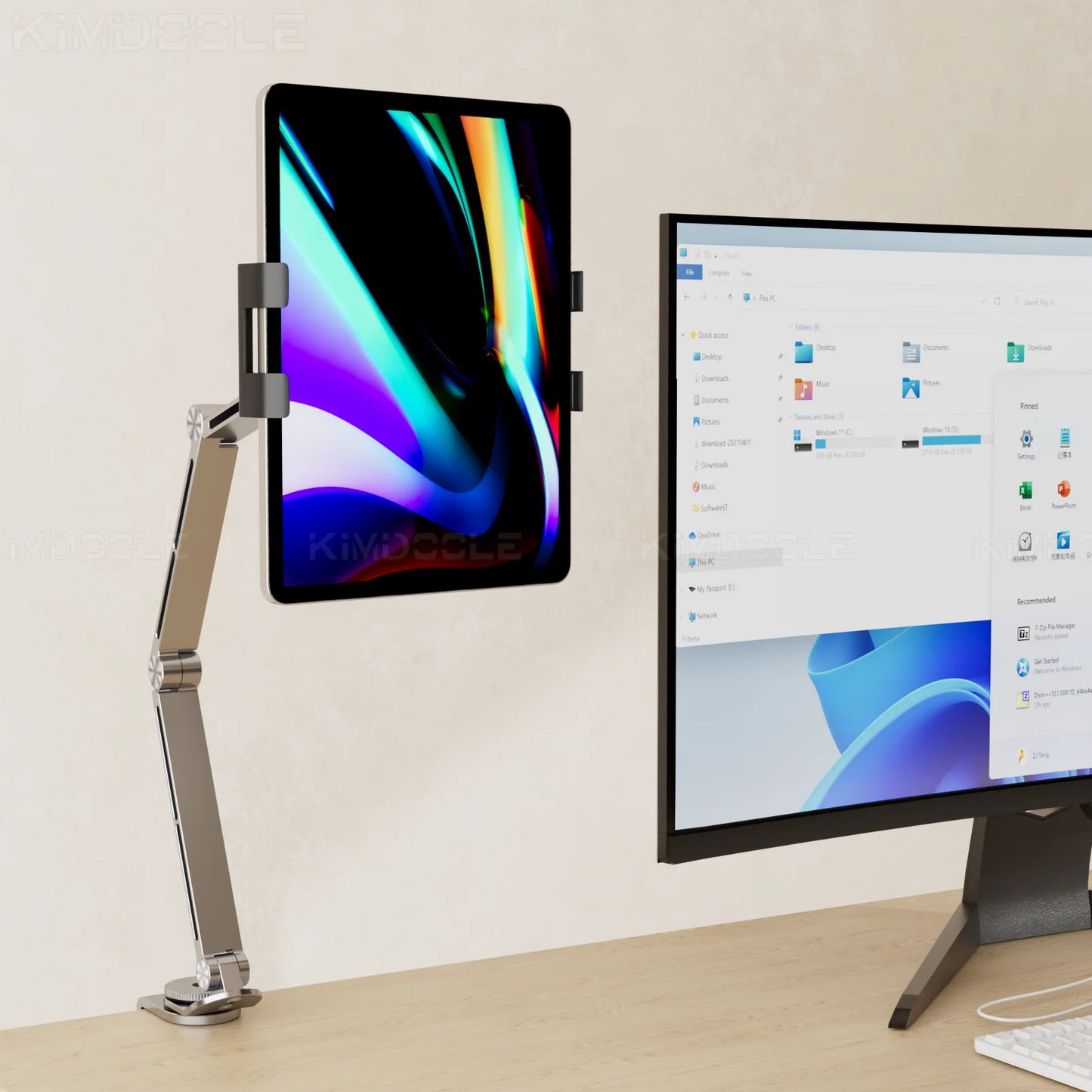The Artpowers Adjustable Tablet Holder - Versatile Stand is mounted beside a computer monitor showing a Windows file explorer. This setup elegantly rests on a wooden desk against a neutral-colored wall.