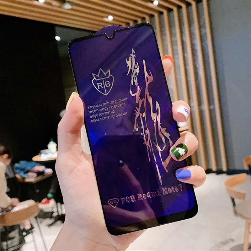 A hand with vibrant, decorated nails holds a Xiaomi phone protected by the LITBOY Tempered Glass Protector; text and designs reflect on the screen. The backdrop features a stylish café with chairs and tables.