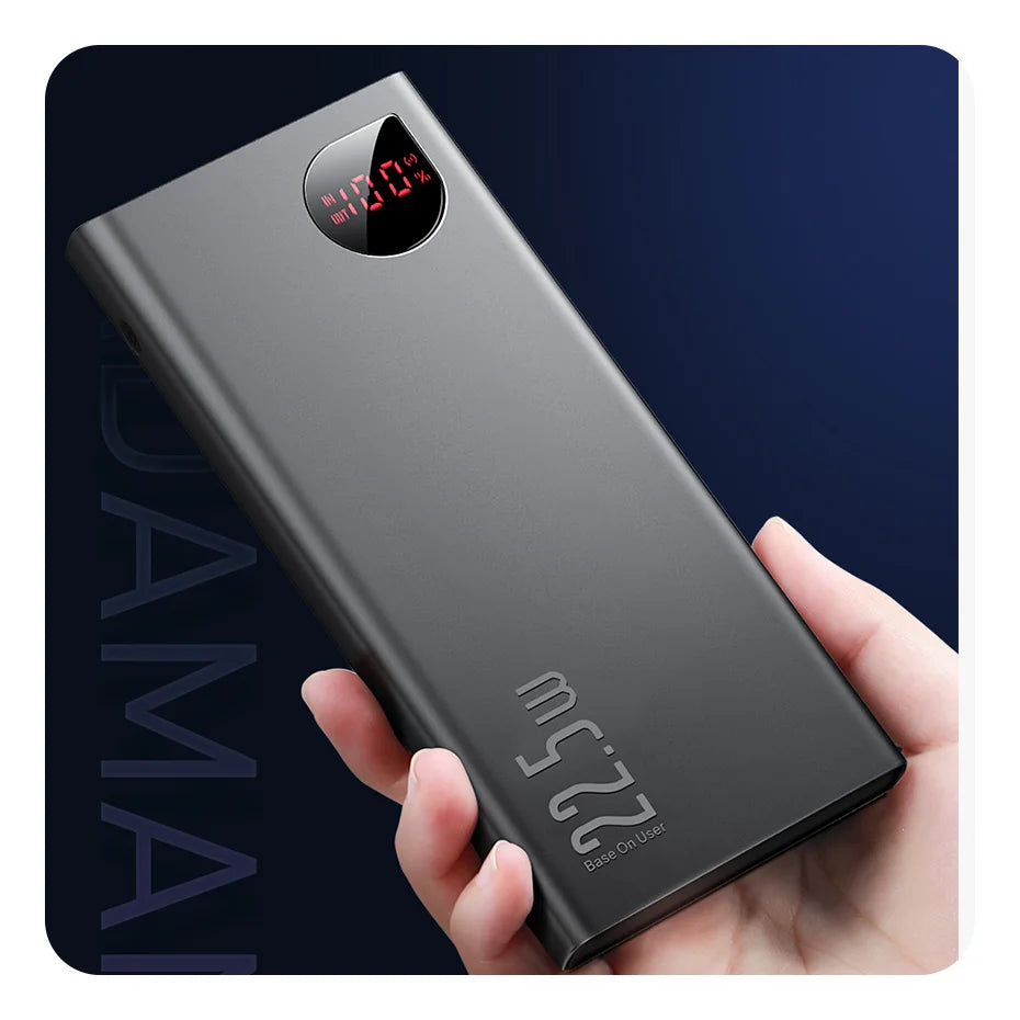 A hand holds a sleek, rectangular black Baseus 10000mAh Power Bank with fast charging and a digital display showing 99%, set against a dark blue gradient background.