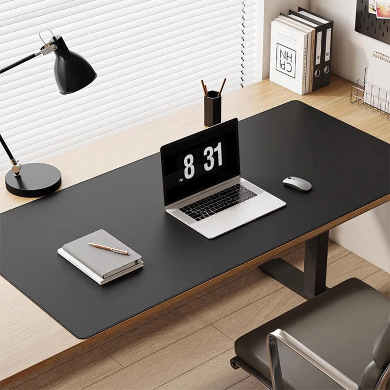 A minimalist office desk setup includes an AIPHY Large PU Leather Mouse Pad - Stylish Waterproof Mat, a laptop showing 8:31, a mouse, stacked notebooks, pens in a holder. A black lamp illuminates books by the window with blinds.