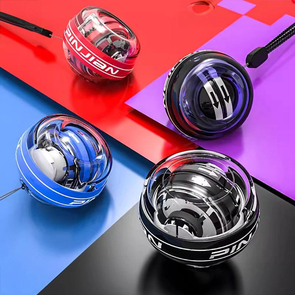 Four transparent gyroscopic exercise balls with colored bands (red, black, blue) sit on a red, blue, purple, and black panel surface. The Wrist Trainer Self-starting Gyro Ball for Strength features adjustable intensity and includes a string for spinning.