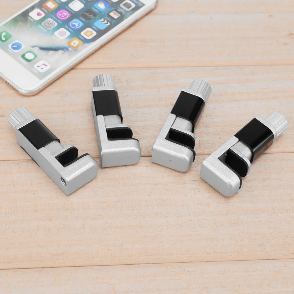 Four silver and black cable organizers rest on a wooden surface next to a smartphone with a colorful app. A MOJOYCE Adjustable Alloy Clamp for Secure Mobile Repairs subtly emphasizes the harmony of functionality and modern design.
