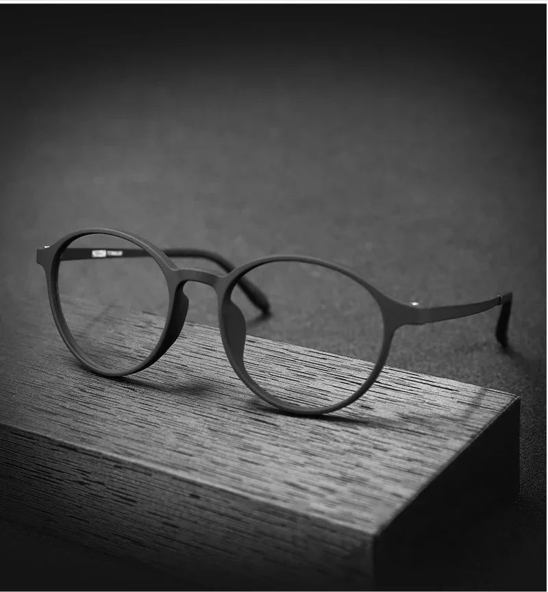 The OUTMIX Pure Titanium Anti Blue Light Reading Glasses are elegantly displayed on a rectangular wooden block against a dark backdrop, their minimalistic and modern design highlighted by subtle reflections off the titanium frame and lenses.