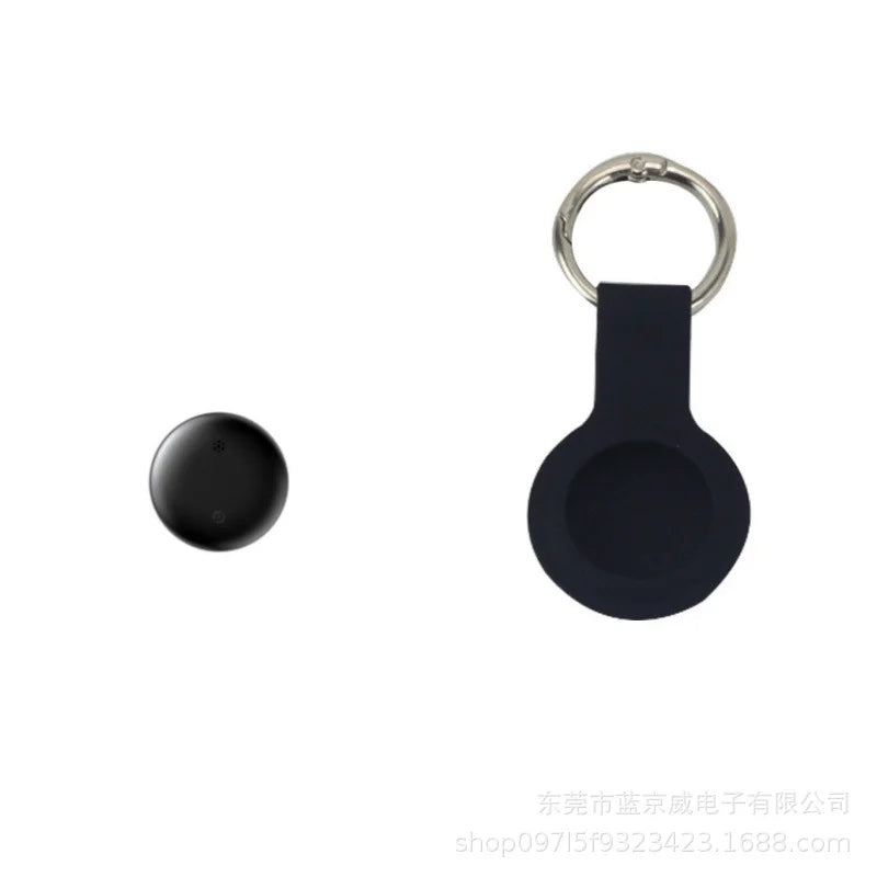 Sitting next to its matching holder with a silver keyring, the sleek black round NoEnName GPS Tracker - Bluetooth Locator for Pets features a minimalist design that integrates seamlessly into the holder, standing out against the plain white background.