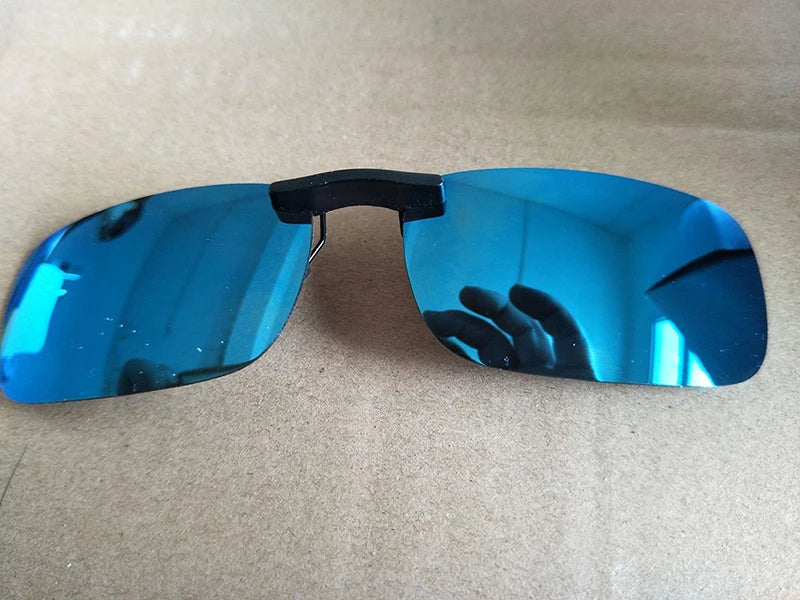 The Honey Joe Polarized Clip-On Sunglasses offer UV400 protection with rimless, rectangular blue-tinted lenses and a black bridge, reflecting a hand and ceiling lights on a beige surface.