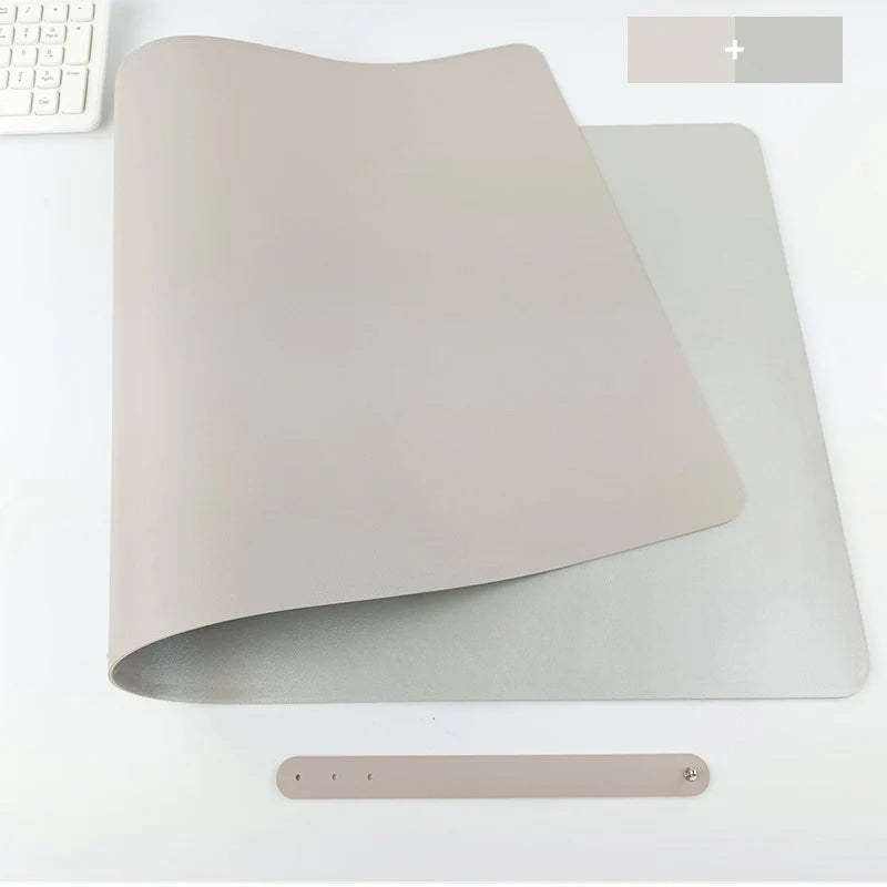 On a white surface, a beige Xummen Large Mouse Pad is rolled up at one end with a small strap and button beneath it. A keyboard corner peeks from the top left. The Waterproof PU Gaming Desk Mat offers durability and features a non-slip base for stability.