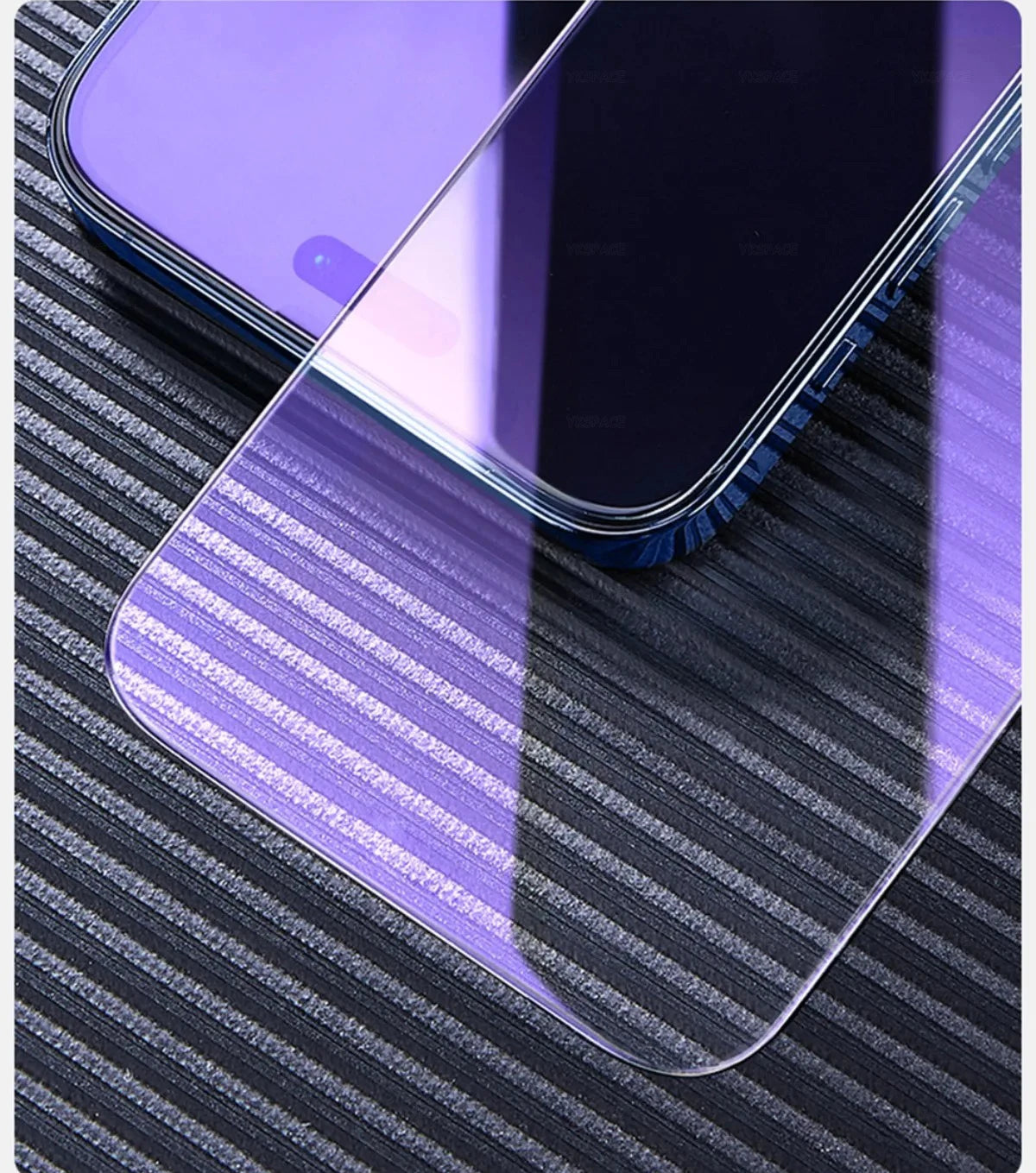 A close-up of a smartphone partially covered by a YKSPACE 2Pcs Anti Blue-Ray Tempered Glass Screen Protector, placed on a textured, dark-striped surface.