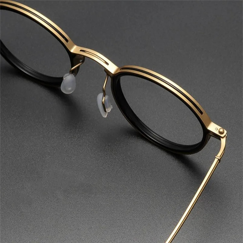 Close-up of KLASSNUM Mens Round Glasses showcasing a gold metal frame with black circular lenses, resting on a dark gray surface. The sleek design includes anti blue light lenses for extra comfort.