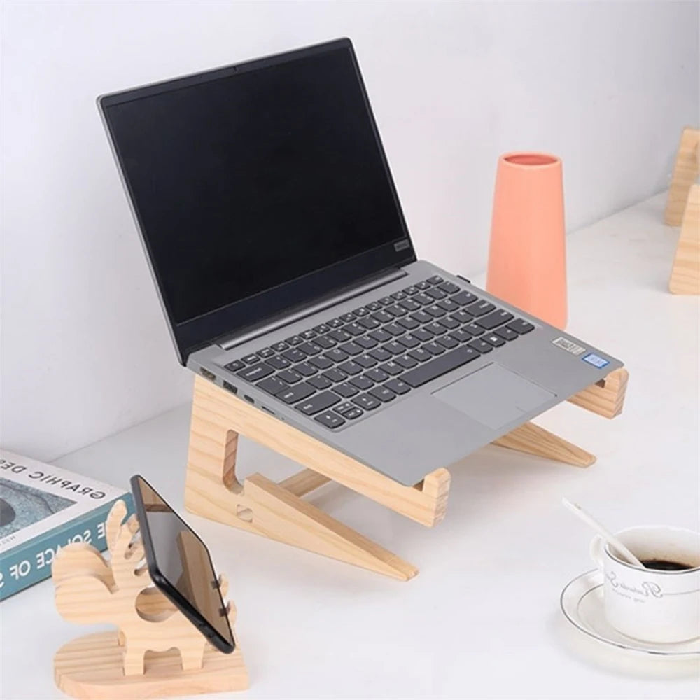 A laptop sits on the Universal Wooden Laptop Holder with a detachable stand next to a cactus-shaped smartphone holder on a white table, accompanied by a cup of coffee, an orange vase, and an open book. Enjoy free shipping on this chic arrangement!.