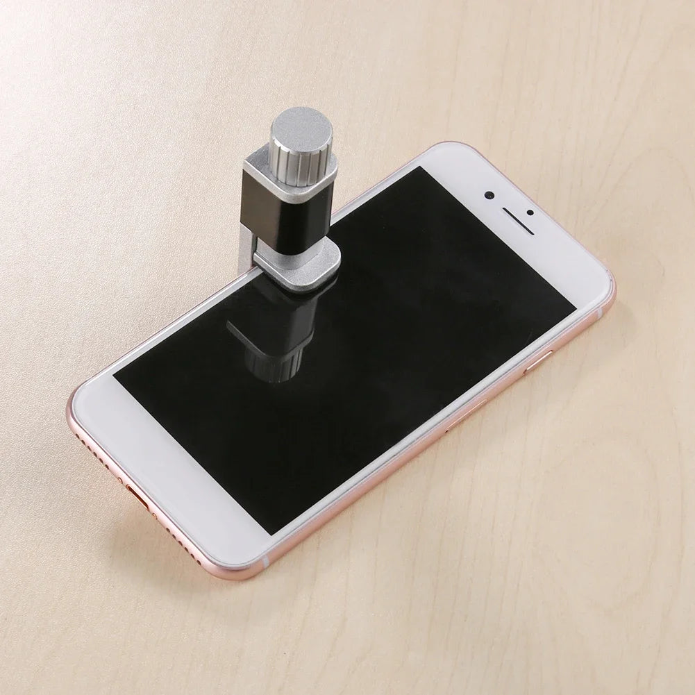 A smartphone with a rose gold frame sits on a light wooden surface, complemented by the MOJOYCE Adjustable Alloy Clamp for Secure Mobile Repairs, holding a sleek silver microscope over its camera. The phones untouched black screen highlights the need for dependable screen protection.