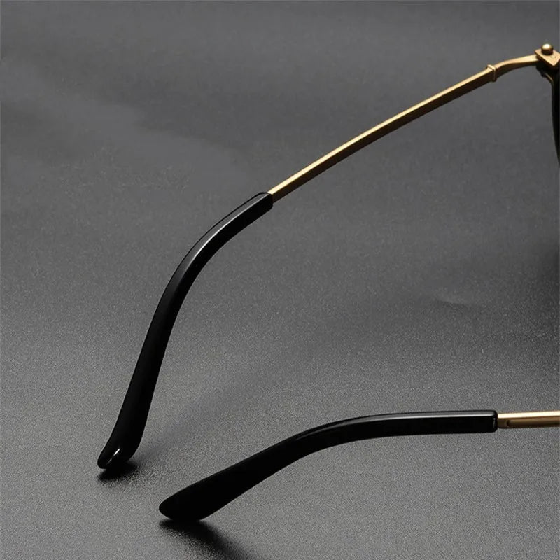 Close-up of KLASSNUM Luxury Round Frame Reading Glasses with gold frames and black earpieces on a dark surface. The focus is on the thin metal arms and curved earpiece tips, highlighting their stylish round frame reminiscent of reading glasses.