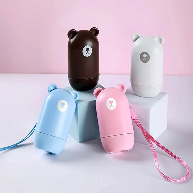Four NoEnName Roller Stamp - Quick Drying Privacy Seal containers in brown, white, blue, and pink are shown on a pastel background. The blue and pink have matching wrist straps. All feature simple bear faces—plus get free shipping!.