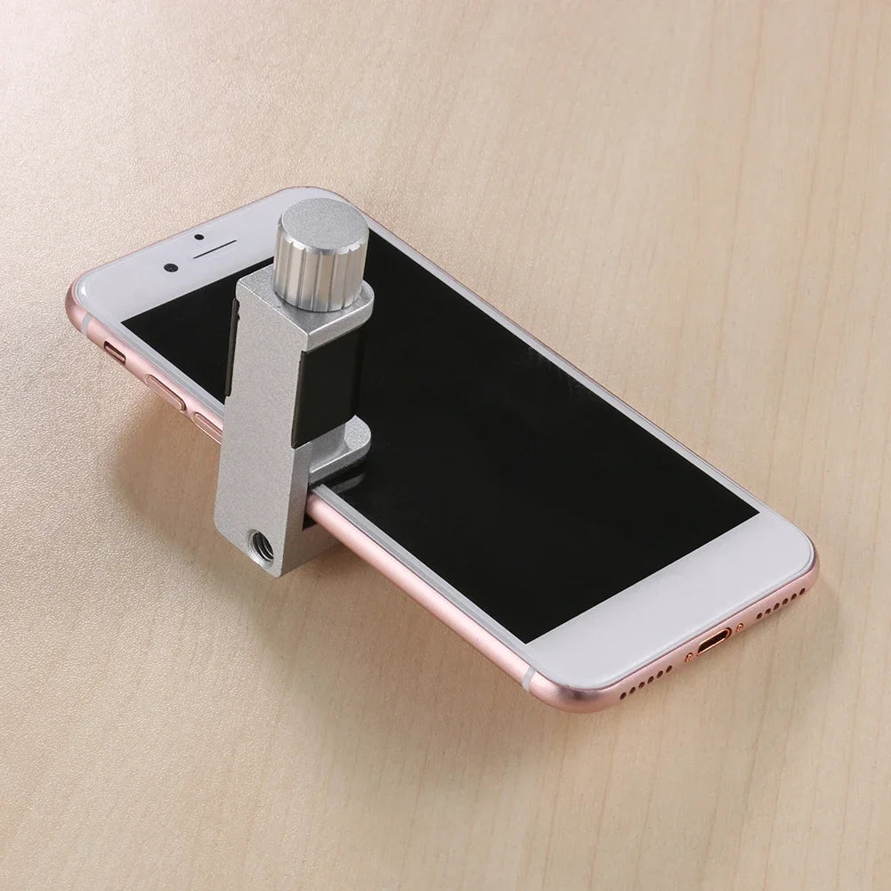 The rose gold smartphone on a wooden surface is held securely by the gray MOJOYCE Adjustable Alloy Clamp, complete with a knob for precision grip, blending style and function in screen protection and mobile repairs.