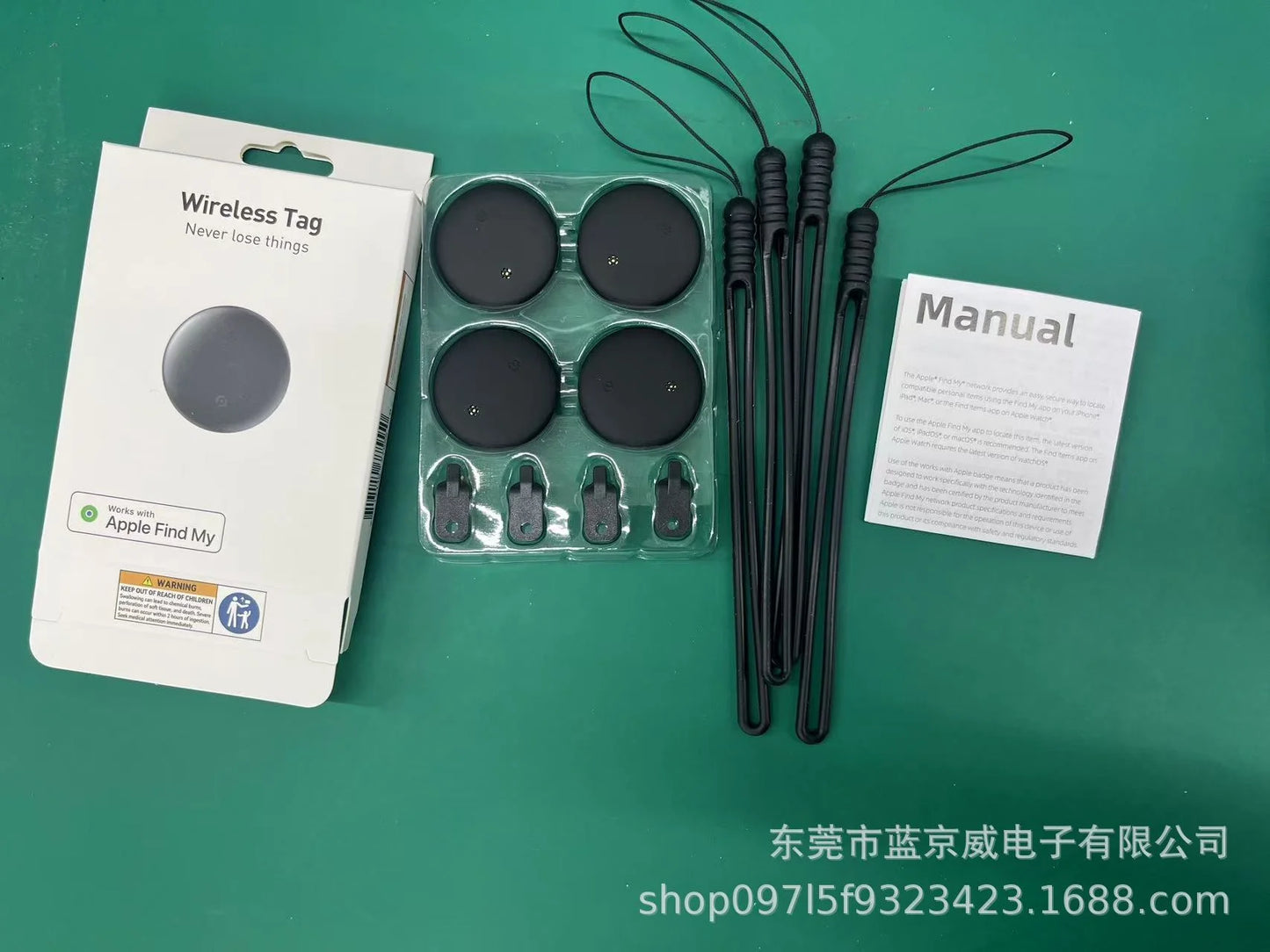 A green surface holds a NoEnName GPS Tracker package with a Wireless Tag box, round tags, a manual, black wrist straps, and keychain attachments. The packaging states compatibility with the Find My App Locator for better tracking. Contact details are printed on the surface.