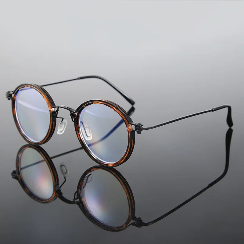 KLASSNUM Mens Round Glasses, featuring round frames with black and tortoiseshell accents, have anti-blue light lenses with a slight blue tint. These stylish retro glasses are displayed on a reflective surface, highlighting their sleek, modern design against a neutral background.