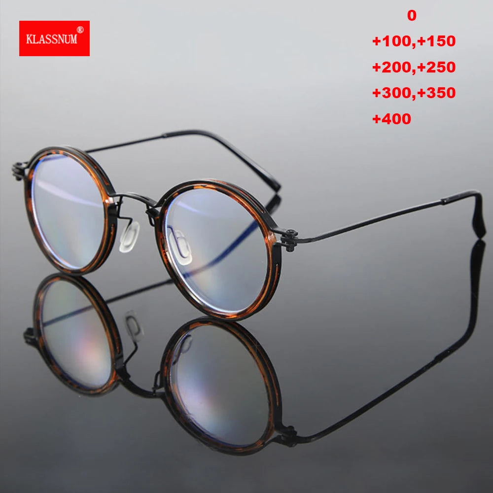 Round eyeglasses with black and brown frames sit on a reflective surface. In the top right, red text lists magnifications from +100 to +400, ideal for reading. The KLASSNUM logo, known for high-quality reading glasses and blue light blocking, is displayed in the top left corner.