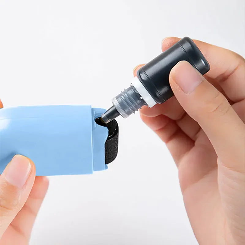 A person refills the NoEnName Roller Stamp - Quick Drying Privacy Seal by squeezing quick drying black ink from a small bottle into its ink pad compartment.