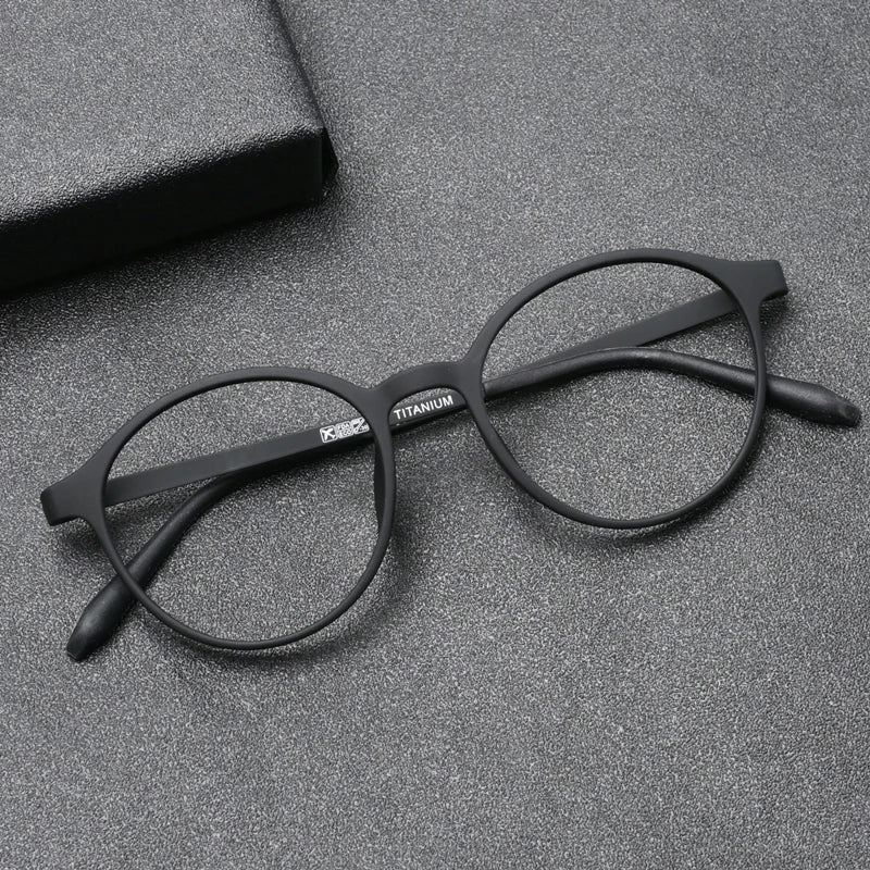 The OUTMIX Pure Titanium Anti Blue Light Reading Glasses, with round black frames, rest on a textured gray surface beside a matching black case. These stylish glasses offer elegance and eye protection, ideal for modern readers.