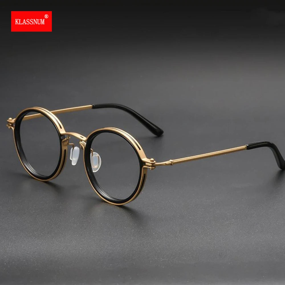 KLASSNUM Luxury Round Frame Reading Glasses - Anti Blue Light feature gold frames with black accents on a dark surface. Slender arms have black tips, and the red KLASSNUM logo on the top-left corner enhances their elegance.