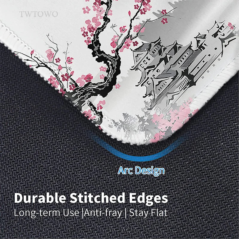 Close-up of the TWTOWO Sakura XL Mouse Pad showcasing its cherry blossom design with a traditional building. It features durable stitched edges, an Arc Design for long-term use, and text that reads: Non-slip surface | Anti-fray | Stay Flat.