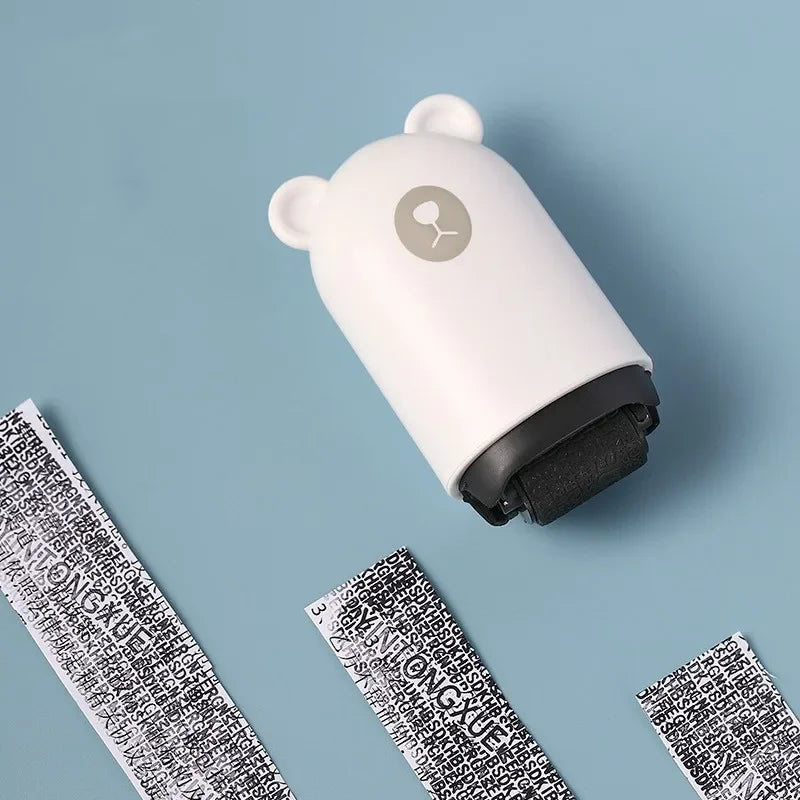 The NoEnName Roller Stamp - Quick Drying Privacy Seal, shaped like a white bear, rests on a blue surface beside paper strips covered with black scrambled text, showing its use in masking printed information.