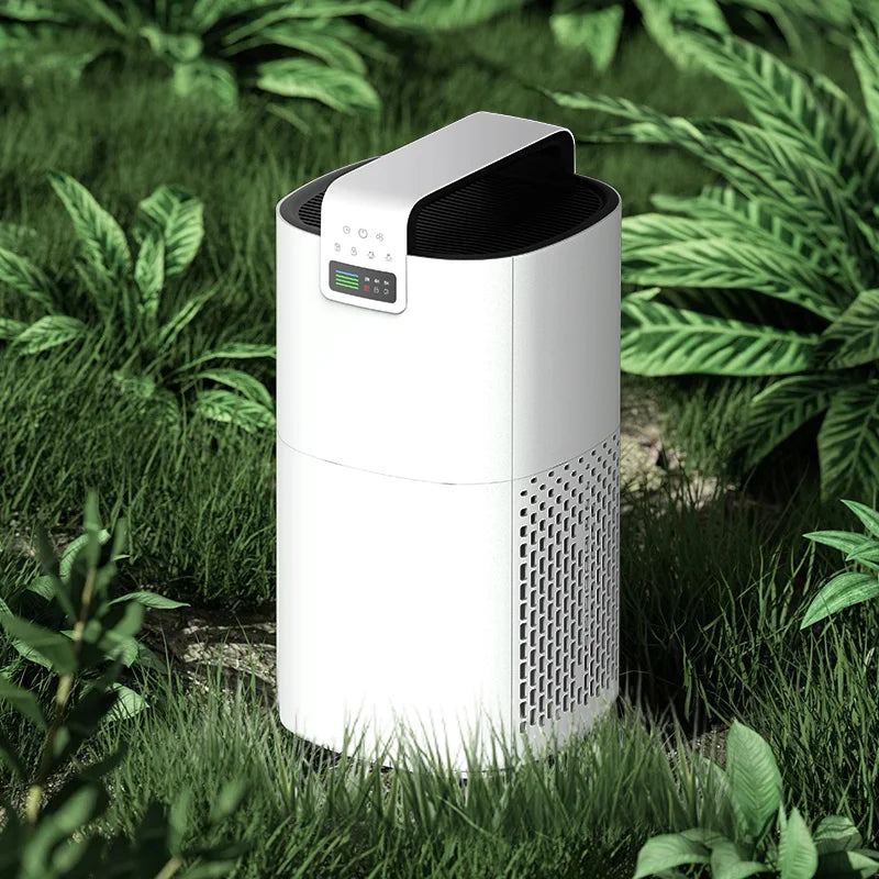 A white, cylindrical JNUO H13 HEPA Air Purifier for Smoke and Aromatherapy with a digital display sits on grass surrounded by lush plants, offering clean air while harmonizing with the serene nearby flora aromas.