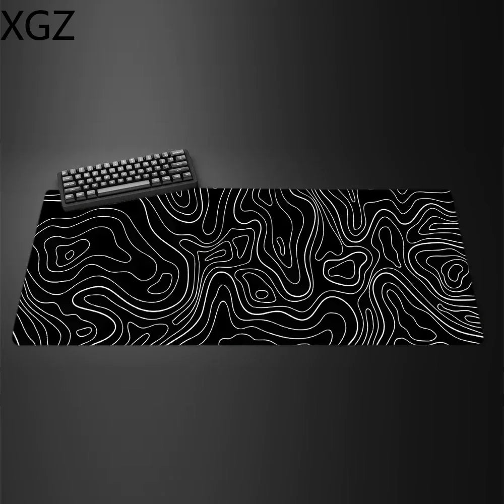 The Large Terrain Map Gaming Mouse Pad, featuring a durable, non-slip surface and white contour lines on a black mat, enhances your setup with its abstract design. Perfect for a dark table, a black keyboard sits in the upper left corner of this stylish accessory.