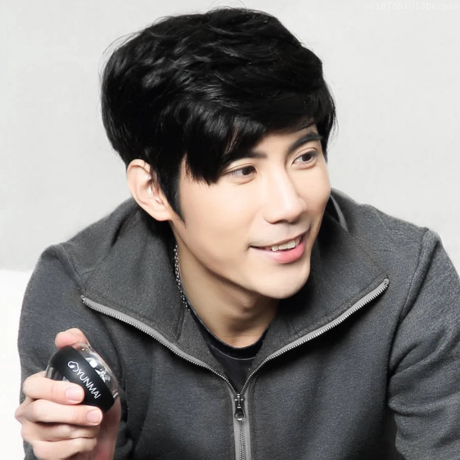 A person with short black hair smiles while holding a small round container, the Xiaomi Forearm Exerciser LED Gyroball Trainer. They are wearing a dark gray zip-up jacket.