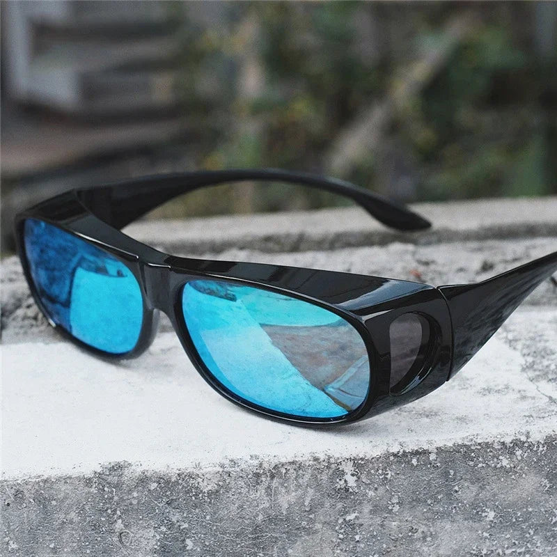 MOKDUFF Polarized Sunglasses with blue reflective lenses sit on a concrete surface outdoors, offering UV400 protection. The background is blurred with hints of greenery.