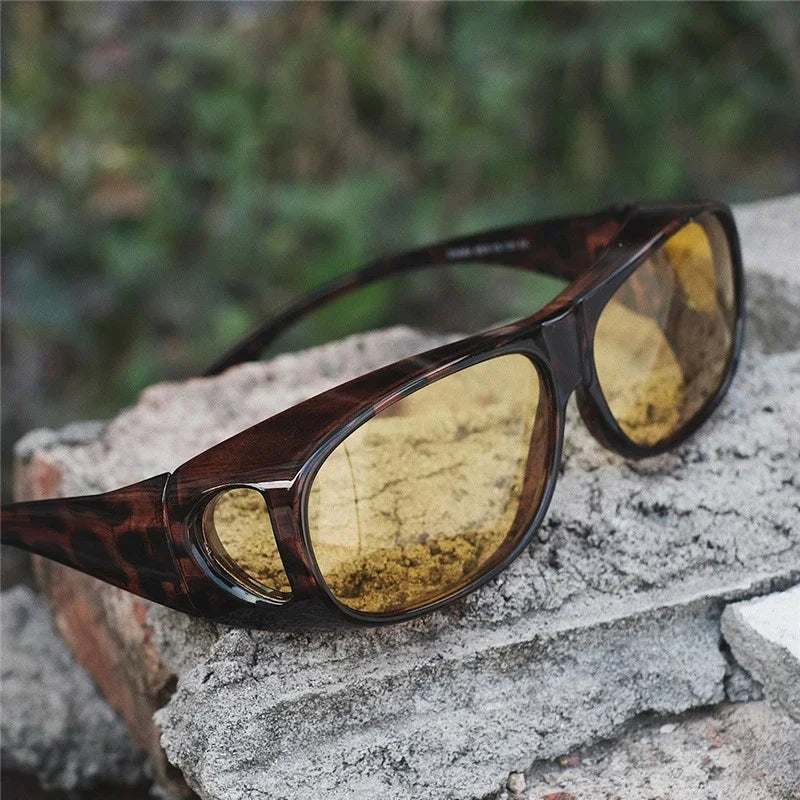 The MOKDUFF Polarized Sunglasses, featuring yellow-tinted lenses and tortoiseshell frames with UV400 protection, rest on a rough stone surface with blurred greenery in the background.
