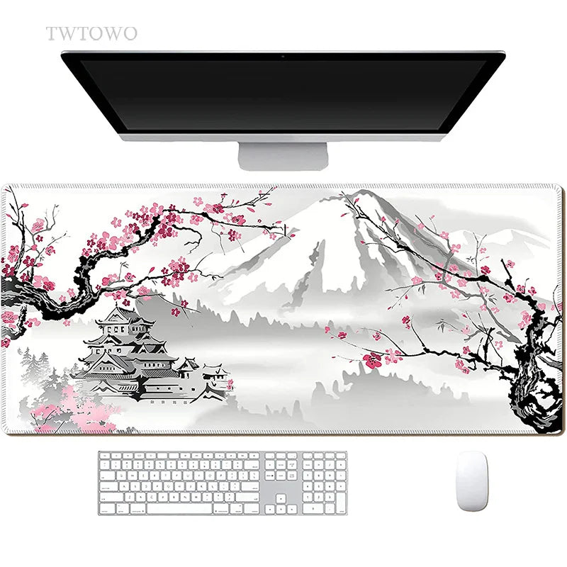 The computer setup includes a TWTOWO Sakura XL Mouse Pad with a non-slip surface, featuring cherry blossoms, a mountain, and a castle. It complements the keyboard and mouse next to the monitor on the pristine white background.
