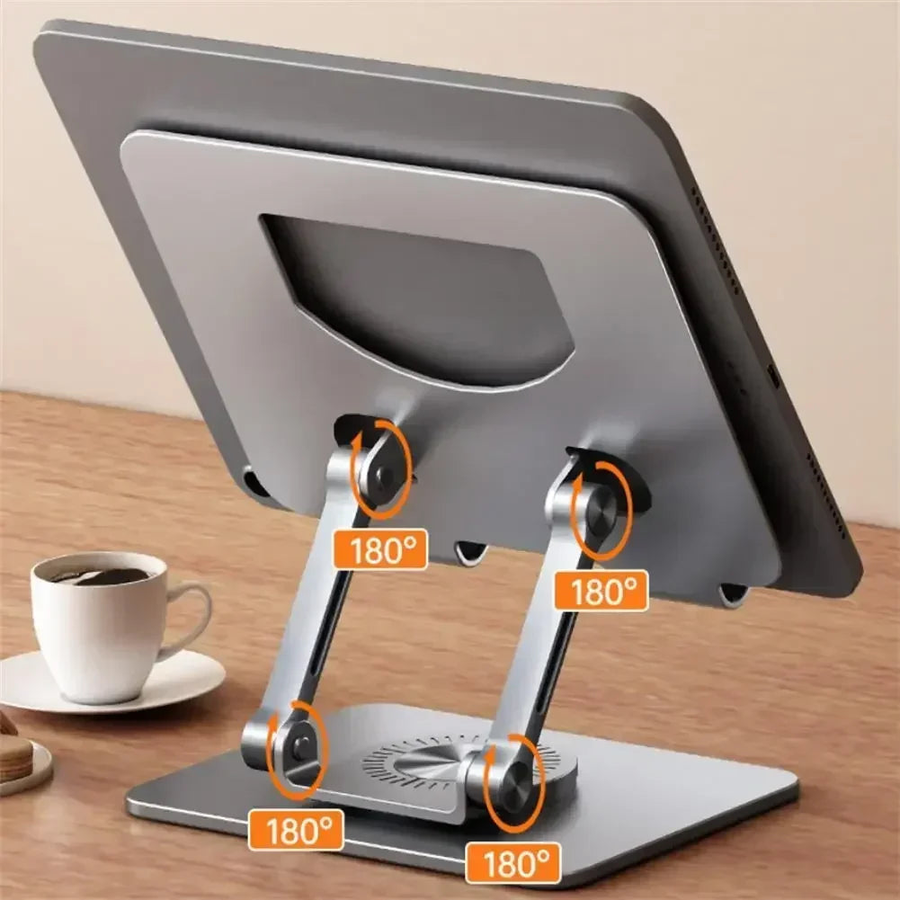 An Adjustable 360° Rotatable Tablet Stand for 4.7-12 devices sits on a wooden desk, showcasing its sleek aluminum design with adjustable hinges and triple-point rotation. A white coffee cup and saucer add to the backdrop.