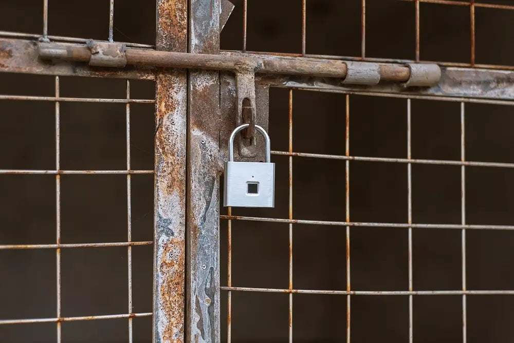 A rusty wire gate is secured with the KERUI Keyless Fingerprint Padlock - Fast 0.2s Waterproof Unlock. The modern padlocks advanced fingerprint technology provides secure access, contrasting against the aged gate and highlighted by a dark background.