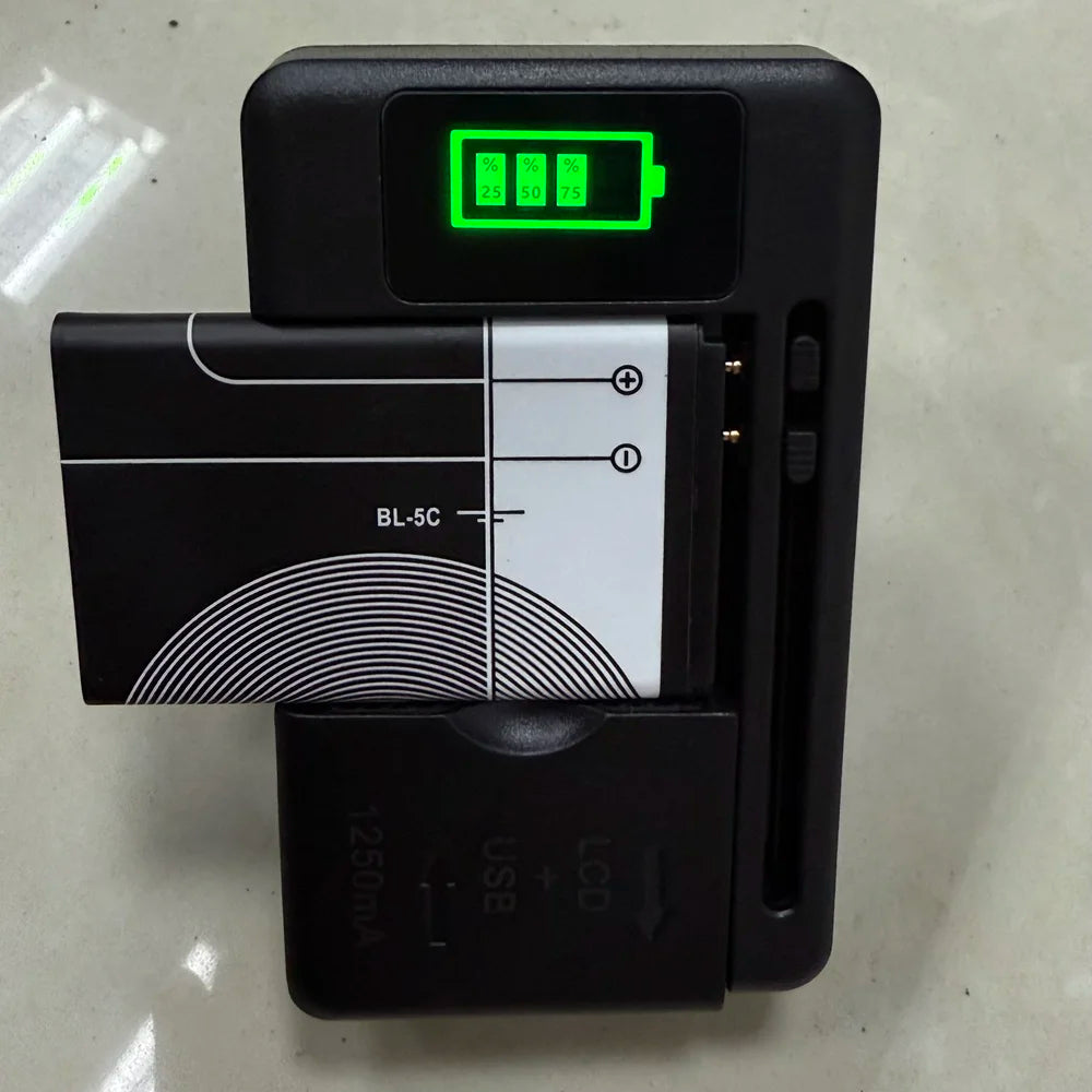 The YIBOYUAN Universal USB Battery Charger, in black, shows charge levels (25%, 50%, 75%) on its LCD. It accommodates a rectangular battery and sits on a light-colored surface.