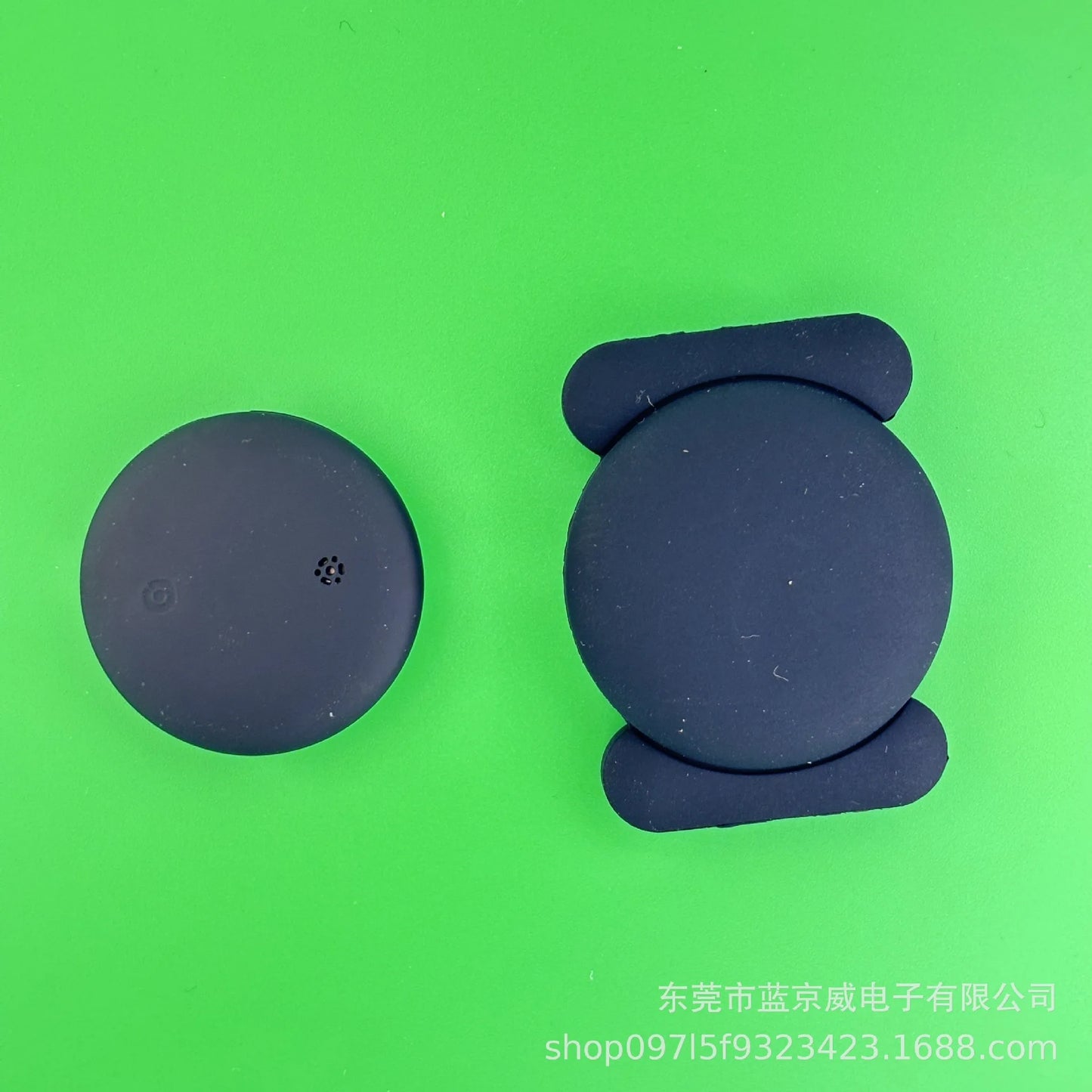 Two black circular smart speaker devices sit against a bright green backdrop. The right device has a flat, cushioned stand. Chinese text and numbers hint at the NoEnName GPS Tracker, a Bluetooth Locator for Pets, ensuring seamless connectivity.