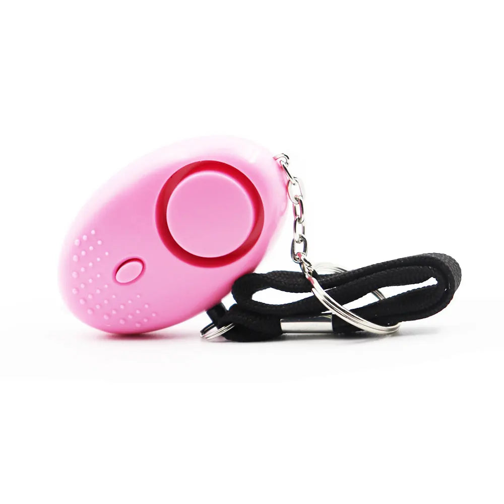 The 130dB Personal Safety Alarm Keychain is a pink, oval-shaped device with a large circular button for self-defense, connected to a black wrist strap by a small metal chain. It includes textured dots, a small on/off switch, and emits 130dB alerts for safety and ease of use.