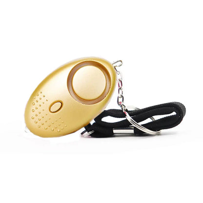 The 130dB Personal Safety Alarm Keychain emits a loud alert and features a gold, oval design with a small button and dotted speaker area. It attaches to a black wrist strap with a metal keyring, making it ideal for self-defense situations.