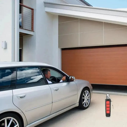 A person in a silver car uses the Universal 433MHz Wireless Remote Control For Garage Access to open a wooden garage door of a modern house.