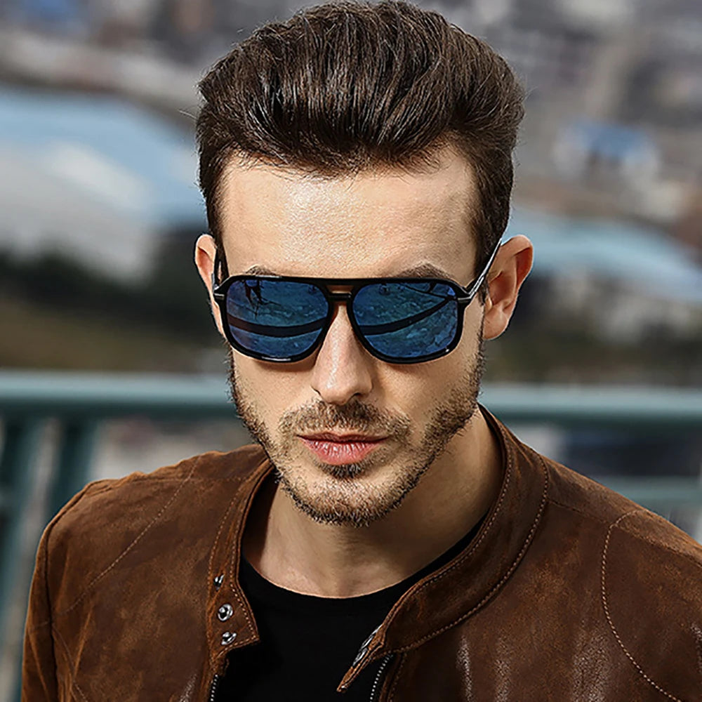 A brown-haired, bearded man stands outdoors in a brown leather jacket, wearing VIVIBEE Mens Polarized Night Vision Glasses - Stylish Clarity. The dark sunglasses suggest a cityscape in the blurred background.