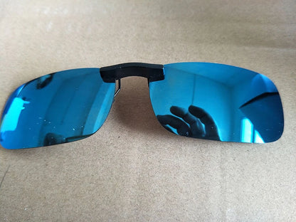 The Honey Joe Polarized Clip-On Sunglasses offer UV400 protection with rimless, rectangular blue-tinted lenses and a black bridge, reflecting a hand and ceiling lights on a beige surface.