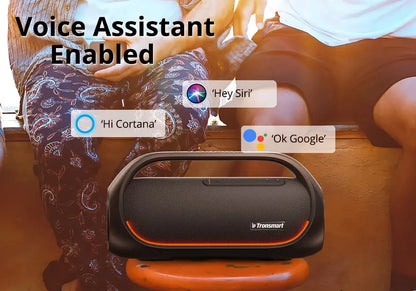 The Tronsmart Bang 60W Bluetooth speaker, featuring heavy bass and app control, rests on a wooden ledge between two people. Text says Voice Assistant Enabled with speech bubbles: Hi Cortana, Hey Siri, Ok Google. It ensures powerful sound in this outdoor scene.