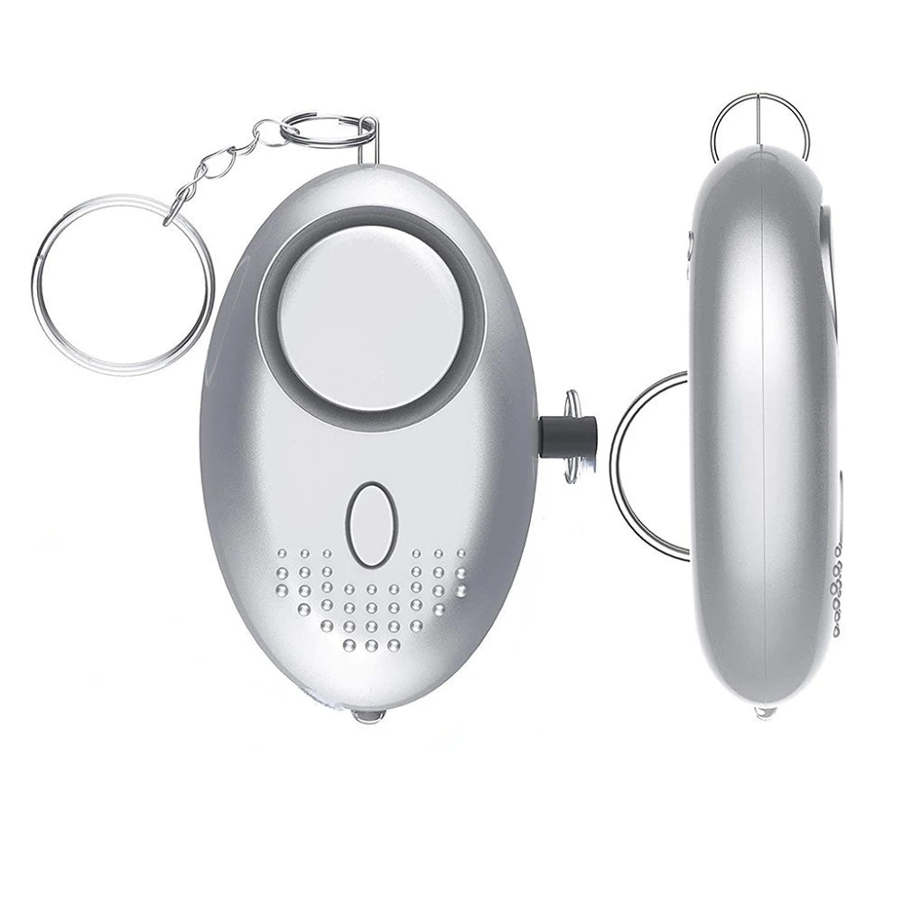 The 130dB Personal Safety Alarm Keychain has a silver oval design with a keychain ring. Its front features a large button and small speaker holes, while the side shows its slim profile. It activates a powerful 130dB alert for self-defense.