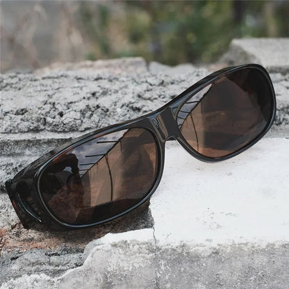 MOKDUFF Polarized Sunglasses, designed for comfortable wear over glasses, in black with wrap-around UV400 protection and dark lenses, are set on a rough rocky surface against a blurred natural background.