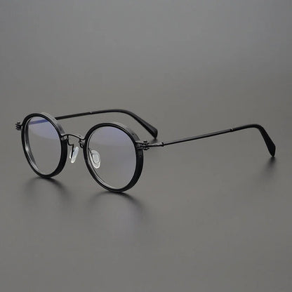 KLASSNUM Mens Round Glasses with retro black frames and anti-blue light lenses sit on a flat, dark gray surface. They have flexible nose pads and sleek temples. The subtle lens reflection adds to their simple, classic appeal, making them ideal mens eyewear.