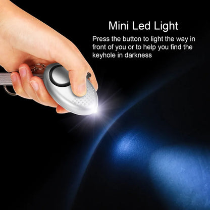 A hand holds a silver mini LED light keychain, serving as a personal safety alarm with a 130dB alert. The text reads: 130dB Personal Safety Alarm Keychain for Instant Alerts. Press to illuminate or activate for self-defense in uncertain situations.