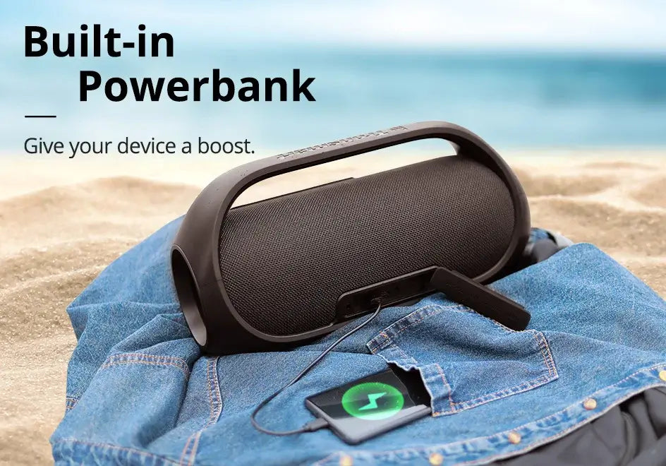 The Tronsmart Bang Speaker, a 60W Bluetooth device with heavy bass and app control, powers up the beach vibe while charging a smartphone on a blue cloth, with the text above reading: Built-in Powerbank: Give your device a boost.