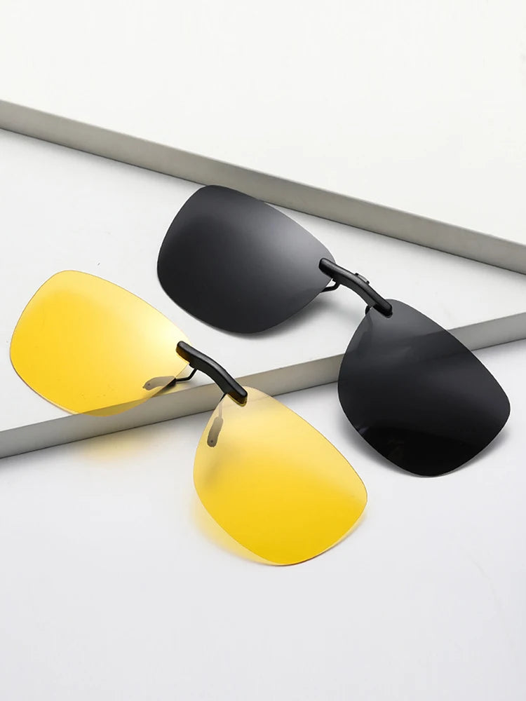 Two pairs of Polarized Clip-On Sunglasses with UV400 Anti-Glare Protection lie diagonally on a white surface. Both have black frames; one has dark lenses, and the other features yellow lenses, designed in a sleek, minimalistic style.