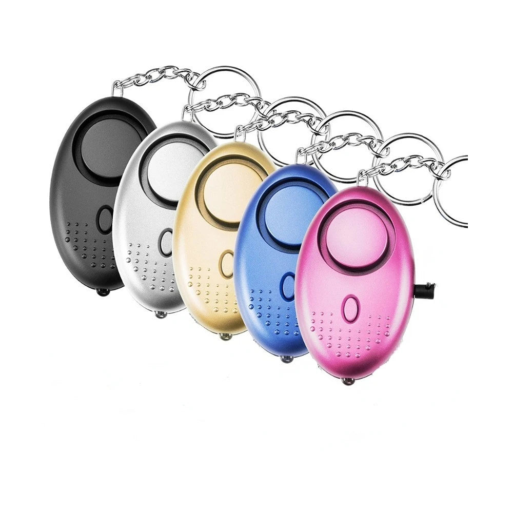 Five oval-shaped, 130dB Personal Safety Alarm Keychains in black, silver, gold, blue, and pink are arranged in a row. Each features a circular button with textured dots below—perfect for self-defense.