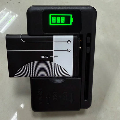 The YIBOYUAN Universal USB Battery Charger, in black, shows charge levels (25%, 50%, 75%) on its LCD. It accommodates a rectangular battery and sits on a light-colored surface.