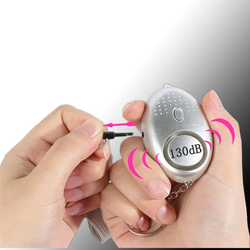 A hand grasps the 130dB Personal Safety Alarm Keychain, its pin pulled for self-defense. Emitting pink sound wave graphics to illustrate its intense alertness, it hangs from a keychain strap, offering peace of mind and personal safety.